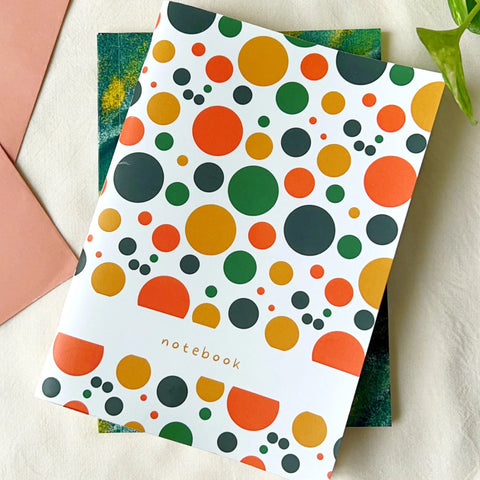 Eco-friendly notebook with colorful circle patterns in orange, green, and mustard on white cover, placed on textured fabric