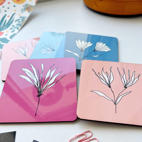 Set of colorful eco-friendly square coasters with minimalist white floral designs on pink, blue, and peach backgrounds