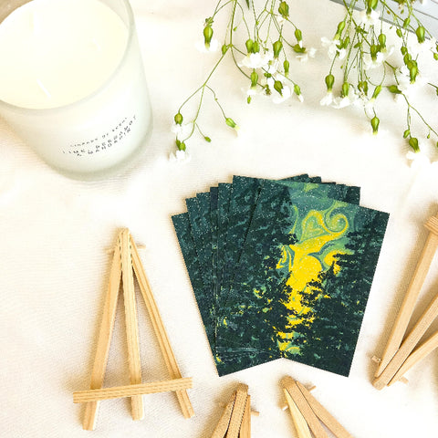 Stack of green and yellow cards with a forest design on a white surface with wooden stands.