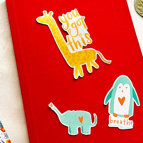 Red notebook with inspirational animal stickers: giraffe you got this, teal elephant, and penguin with breathe text