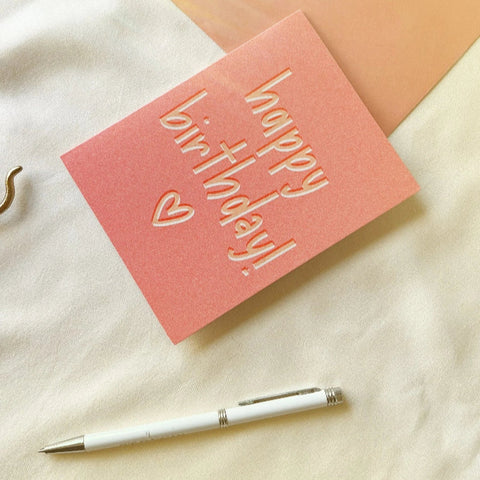 Aesthetic pink birthday card flatlay with pen and green art paper.