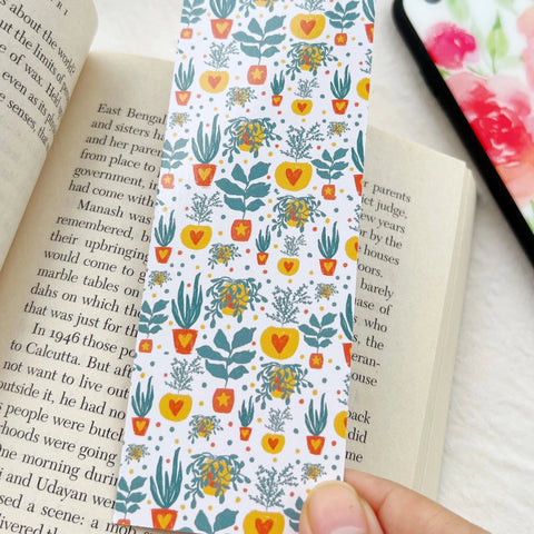 "Hand holding a floral bookmark with green leaves and orange hearts"