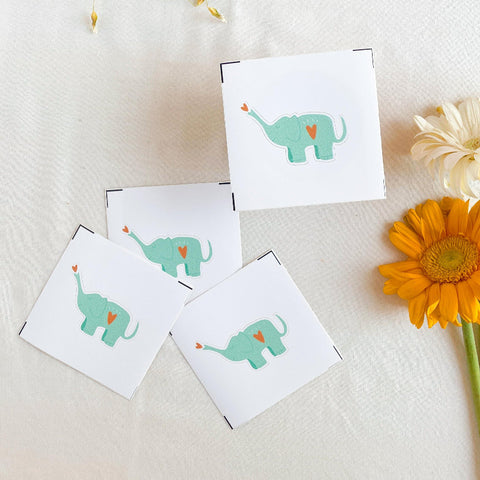Four cards with green elephants on a white surface with flowers.