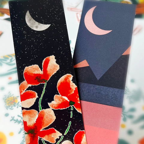Hand holding moon-themed bookmarks with artistic illustrations