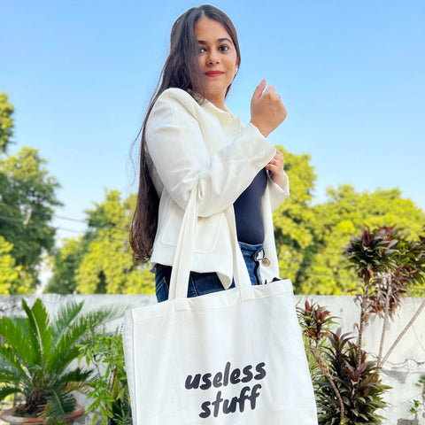 Woman holding a white tote bag with 'useless stuff' text outdoors.
