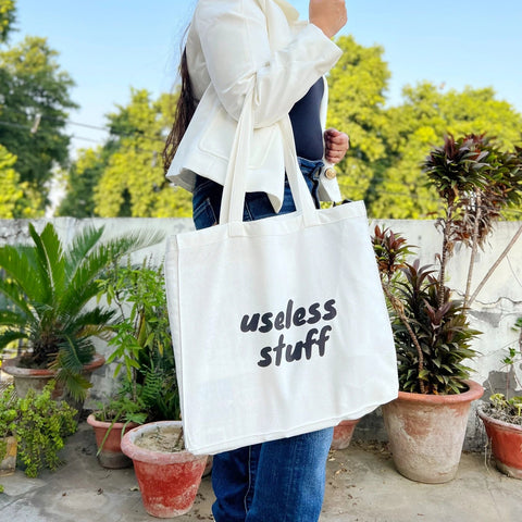 Woman holding a white tote bag with 'useless stuff' text outdoors.