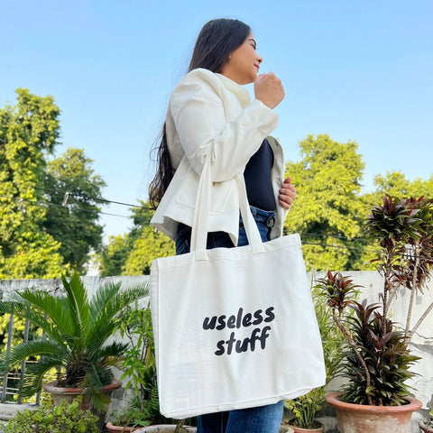 Person holding a tote bag with 'useless stuff' text in an outdoor setting