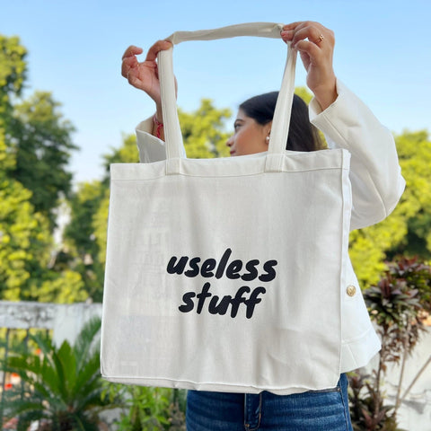 Person holding a tote bag with 'useless stuff' text outdoors