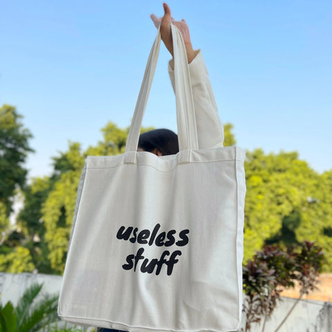 Person holding a tote bag with 'useless stuff' text outdoors
